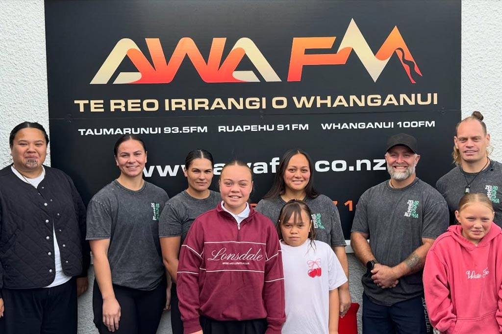A group of people of all ages standing in front of the Awa FM logo